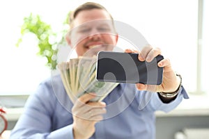 Man making self photo with mobile phone camera posing with pile of money