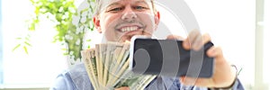 Man making self photo with mobile phone camera posing with pile of money