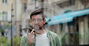 Man making voice message or using virtual assistant app on mobile phone. Young man in glasses recording voice message on