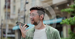 Man making voice message or using virtual assistant app on mobile phone. Young man in glasses recording voice message on