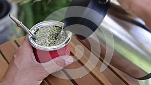 Man making yerba mate tea. Close up pouring hot water into traditional Mate cup. Slow Motion.
