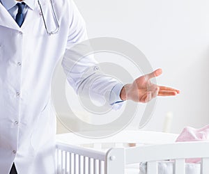 Man male pediatrician near baby bed preparing to examine