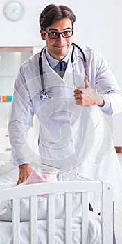 Man male pediatrician near baby bed preparing to examine