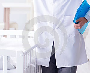 Man male pediatrician near baby bed preparing to examine