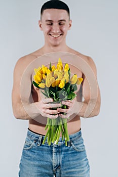 Man man with naked torso gives flowers. Romantic Man with bouquet of tulips for birthday. Happy woman`s day. Giving