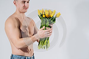 Man man with naked torso gives flowers. Romantic Man with bouquet of tulips for birthday. Happy woman`s day. Giving