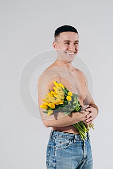 Man man with naked torso gives flowers. Romantic Man with bouquet of tulips for birthday. Happy woman`s day. Giving