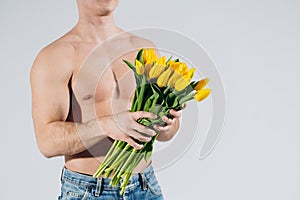 Man man with naked torso gives flowers. Romantic Man with bouquet of tulips for birthday. Happy woman`s day. Giving