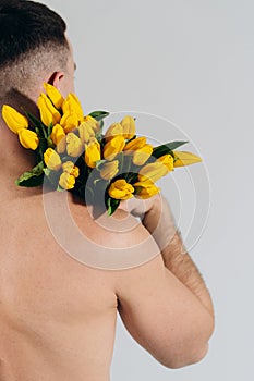 Man man with naked torso holding flowers on shoulder. Back view. Romantic Man with bouquet of tulips for birthday. Happy