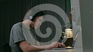 Man man in slouching position listen music on headphones use laptop at night.