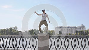 Man in marine uniform, sunglasses show weird gesture, staying on postament at seafront. Surrealism