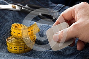 Man marking line with tailor`s chalk on jeans denim fabric with scissors and measuring tape on blue jeans denim close up - jeans