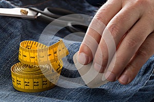 Man marking line with tailor`s chalk on jeans denim fabric with scissors and measuring tape on blue jeans denim close up - jeans