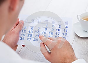 Man marking with pen and looking at date on calendar