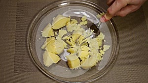 Man mashes potatoes in a glass bowl