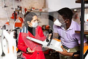 Man in mask consulting woman about chainsaw in store