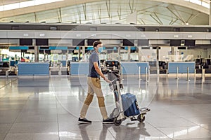 Man in mask at empty airport at check in in coronavirus quarantine isolation, returning home, flight cancellation