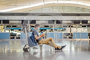 Man in mask at empty airport at check in in coronavirus quarantine isolation, returning home, flight cancellation