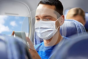 Man in mask sitting in plane with smartphone