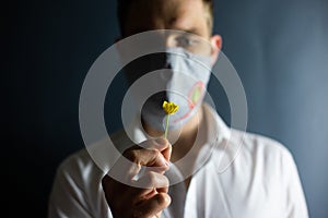 The man in the mask `Stop Coronavirus` sniffs the smell of a fresh flower