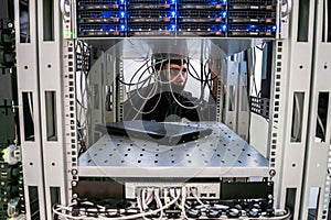 A man in a mask unravels communication cable internet. Hacker switches the wires in the server room. The malefactor is behind the photo