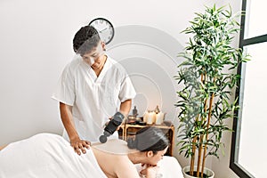 Man massaging woman back using massage gun percusion at beauty center