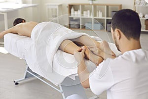 Man masseur chiropractor in white uniform massaging lying relaxing womans heels