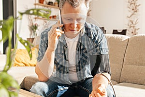 A man measures blood pressure at home with a blood pressure cuff and a tonometer. A man calls a doctor on a mobile phone