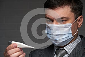 Man measures body temperature with a thermometer, checks his health status, has a protective face mask - healthcare and medicine