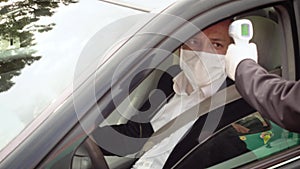 Man measures a driver`s body temperature with infrared thermometer
