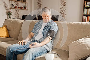 A man measures his blood pressure at home with a cuffed blood pressure monitor. Health check at home. Hypotension or