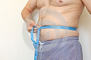 A man measures his fat belly with measuring tape. Concept of weight loss, health problems of obese people. Poor