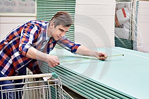 Man measures with roulette drywall sheets in store building mate