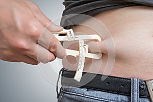 Man is measuring body fat on his belly with caliper