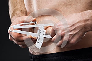 Man is measuring his body fat with calipers.