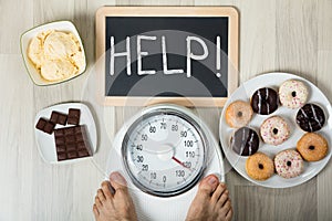 Man Measuring His Weight With Help Sign And Dessert