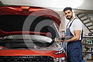 Man mechanic using laptop for auto diagnostics of sport red car engine at the service station