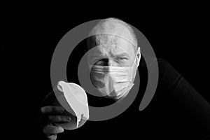 Man in medical face mask and toilet paper roll in hand on black background