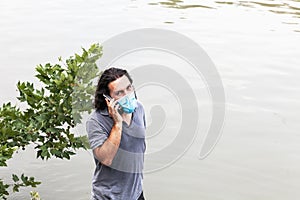 A man in a medical mask on the background a river is talking on the phone