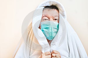 A man in a medical mask covered himself with a housecoat, self-isolation, stay home, fear