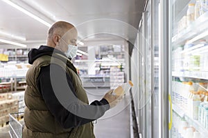 A man in a medical mask in the department with dairy products in a supermarket. Coronavirus pandemic