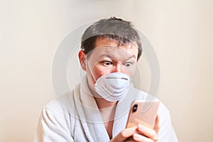 A man in a medical mask and in a dressing gown looks at the phone with surprised eyes, self-isolation, quarantine, stay at home,