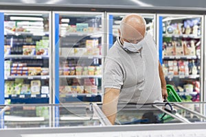 A man in a medical mask in the frozen food section of a supermarket. Coronavirus pandemic