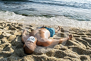 Man in a medical mask gets a tan on the beach at a seaside resort