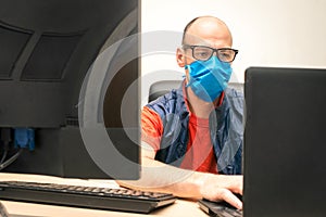 A man in a medical mask and glasses sits in front of monitors. Specialist works at the computer in an individual means of