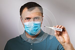 A man in a medical mask holding a thermometer in his hand. The concept of timely verification of body temperature