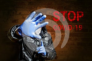 A man in a medical mask holds a hand in a medical glove in front of his face against the background of a stop covid-19