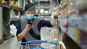 Man with medical mask looking at his mobile phone and shopping in warehouse store during coronavirus covid-19 pandemic