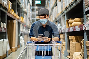 Man with medical mask looking at his mobile phone and shopping in warehouse store during coronavirus covid-19 pandemic