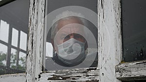 Man In Medical Mask Looks Sadly Out Of Window At Street Because Of The Pandemic